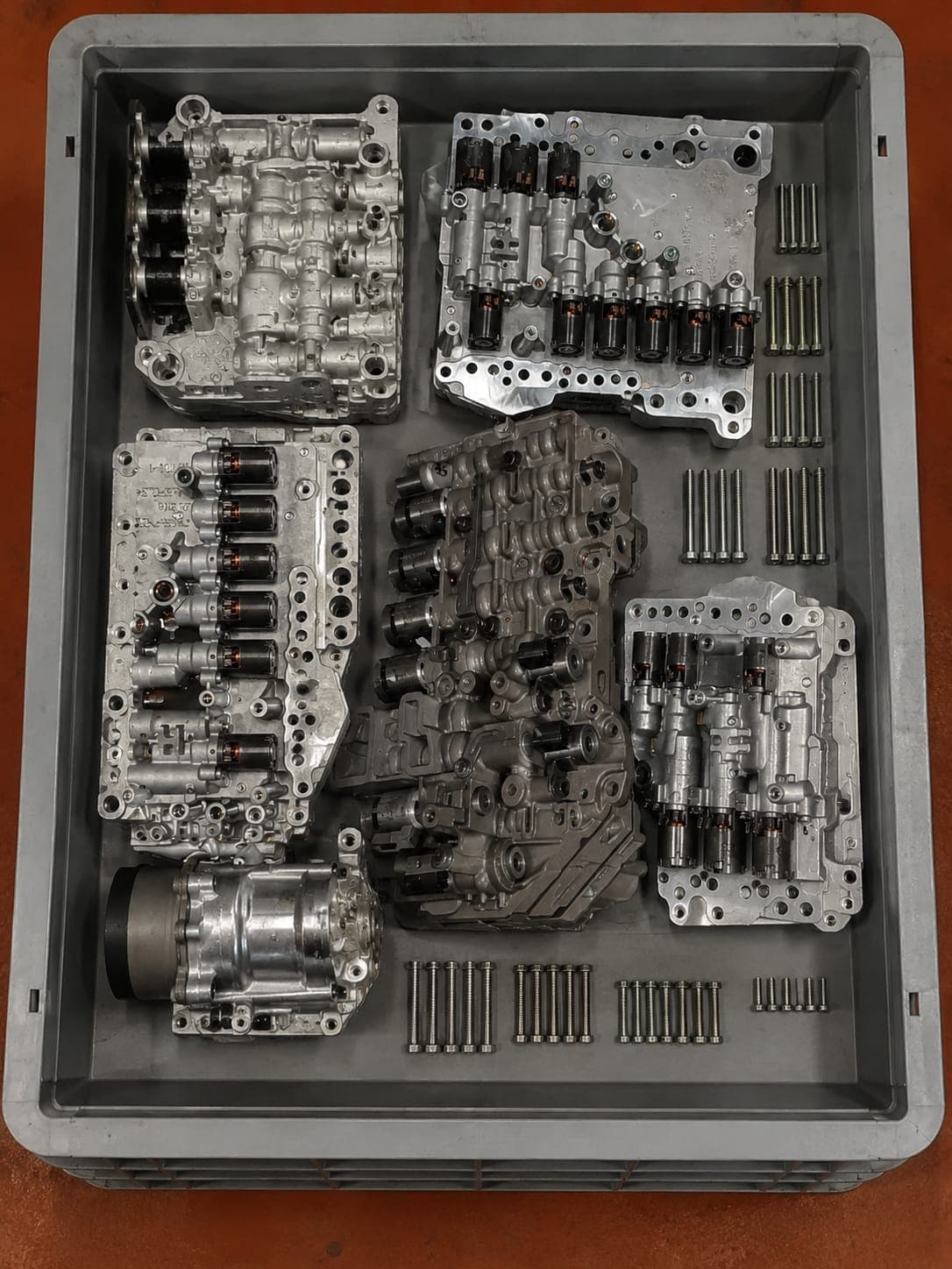 Cuerpos de válvulas y solenoides de mecatrónica organizados en caja de taller tras desmontaje técnico
